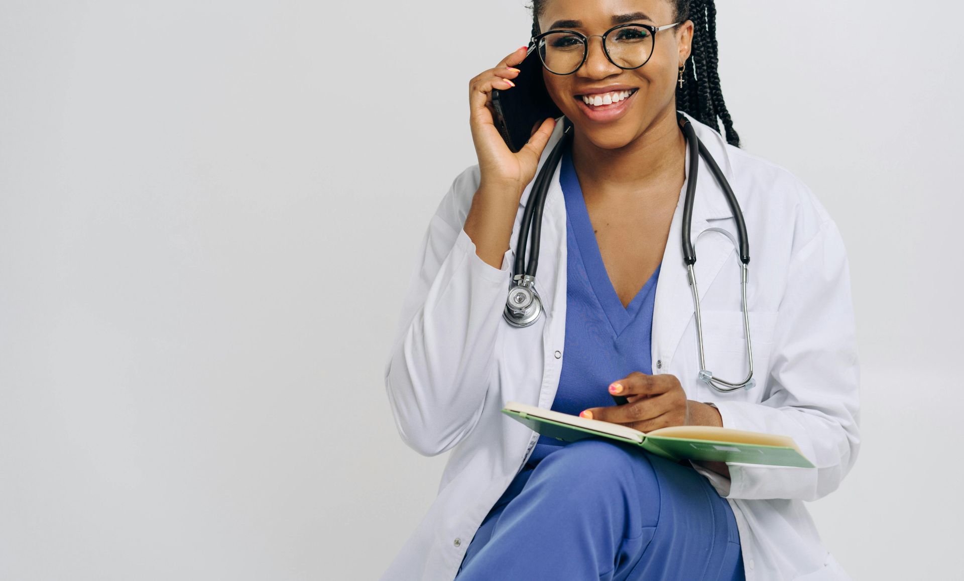 Cheerful female doctor in lab coat talking on smartphone and taking notes.